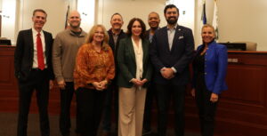 Photo of a City Council members and the City Manager smiling in Council Chambers