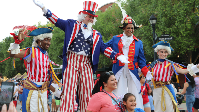 Stilt walkers dressed in patriotic attire, posing with two women
